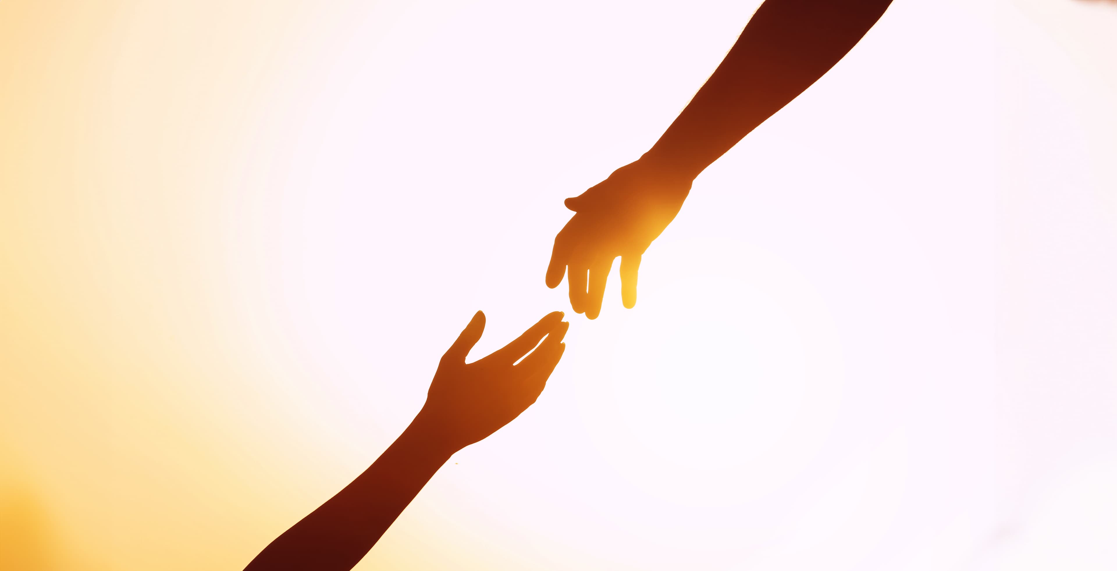 Silhouetted hands reaching toward each other in warm light