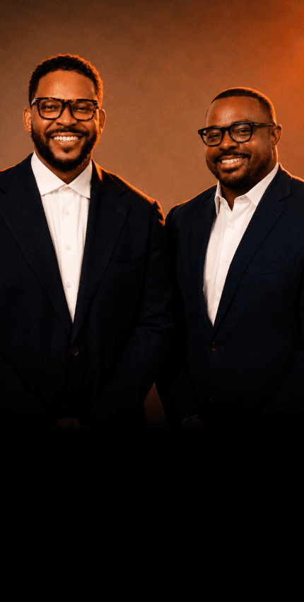 Factory founders Keenan and Travis in tailored suits against a warm studio backdrop