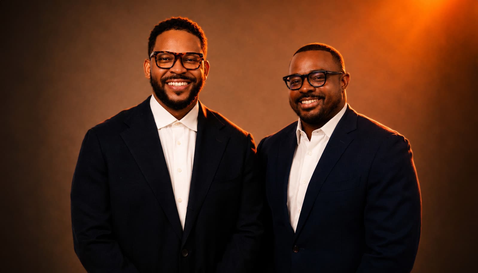 Factory founders Keenan and Travis in tailored suits against a warm studio backdrop