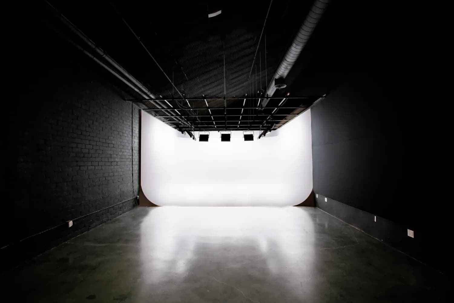 Dark production studio with a white cyc wall and overhead lighting